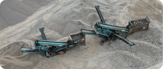 Two large machines positioned atop a substantial mound of sand, showcasing industrial activity in a construction site