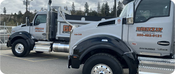 Two large dump trucks parked side by side in a spacious parking lot under clear blue skies