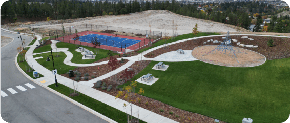 Aerial view of a park featuring a tennis court and a playground, surrounded by lush greenery and pathways