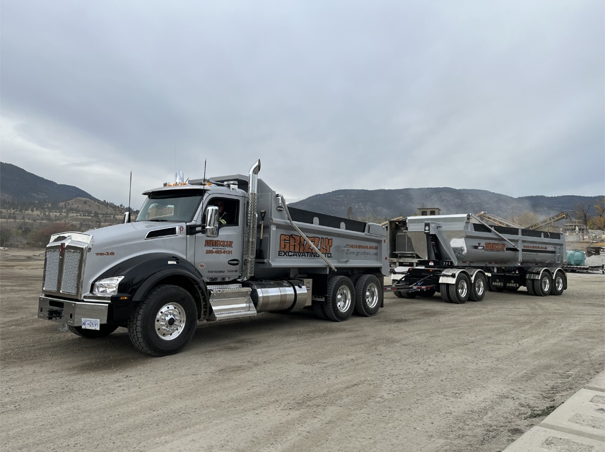 A large dump truck is parked on a dirt road, surrounded by a natural landscape.